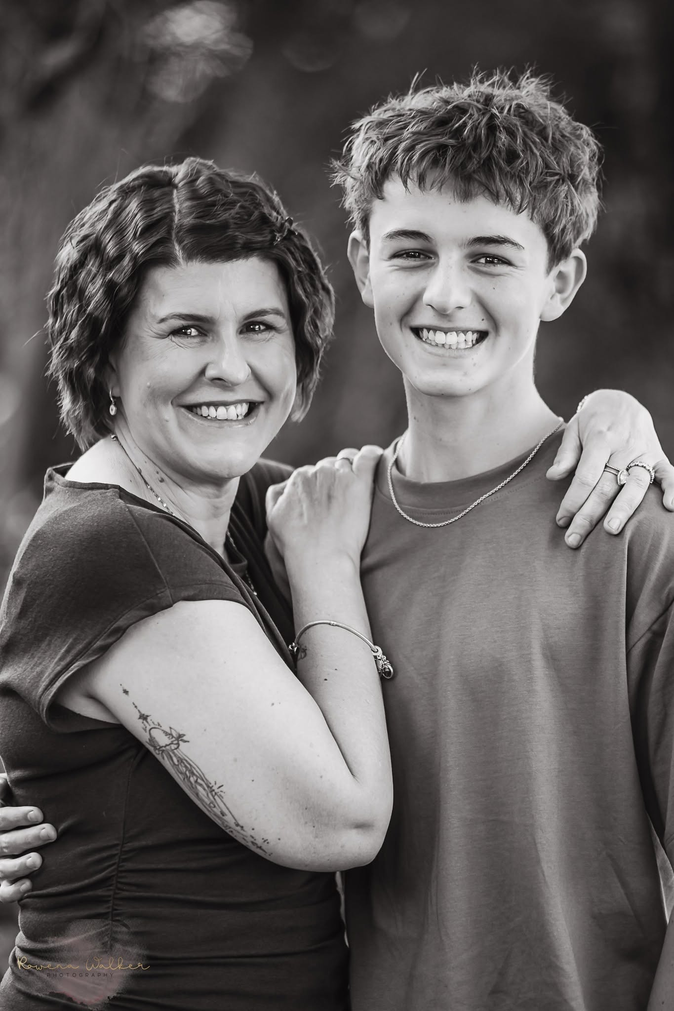Black and white portrait of a smiling mother and her teenage son with his arm around her shoulder